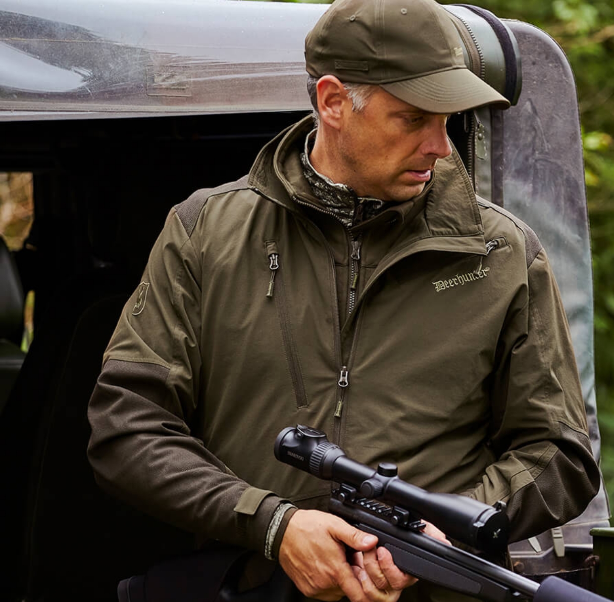 man in deerhunter hat and jacket with rifle